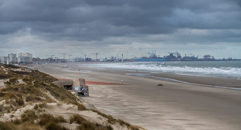 Blockhaus ensablé au pied des dunes de Dunkerque, avec en arrière plan le phare et le port de Dunkerque.